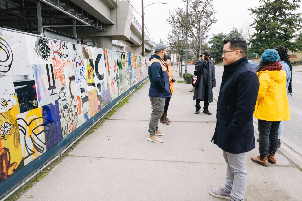 People look at murals on a fence 