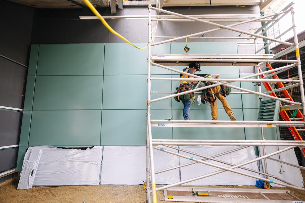 Workers on scaffolding with a blue wall in the background