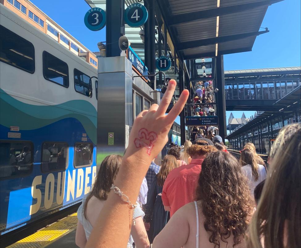 A hand with the number 13 drawn on it is held up in front of a Sounder train