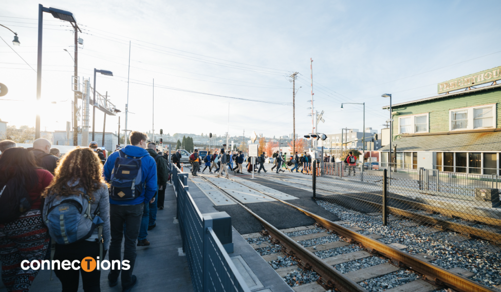 A big group of passengers cross train tracks in Tacoma. Text reads 'connections' with the 'T' emphasized