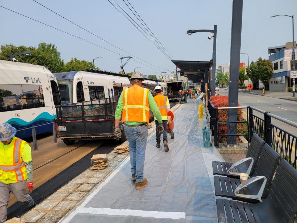 Crews in orange shirts and protective gear work on a Link station platform