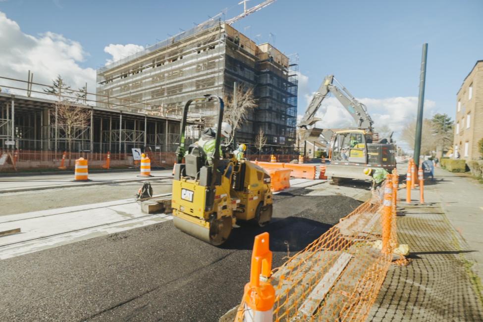 A worker drives a piece of heavy equipment through a construction zone