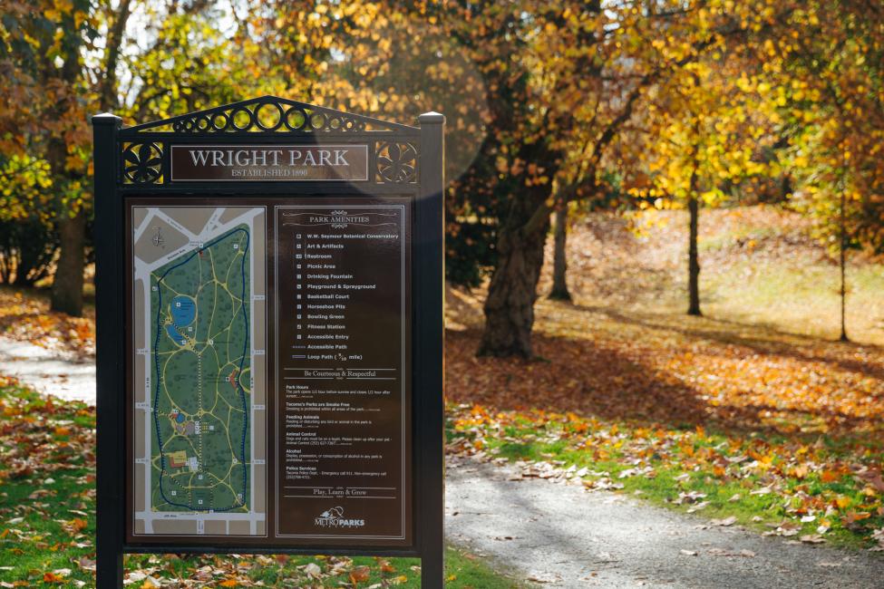 A sign in Wright Park with a map, and a sidewalk and fall colors in the background