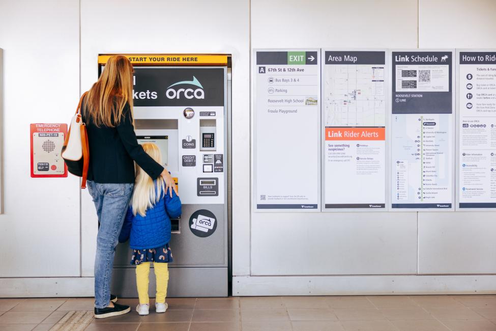 A mother and daughter stand in front of an ORCA ticket vending machine