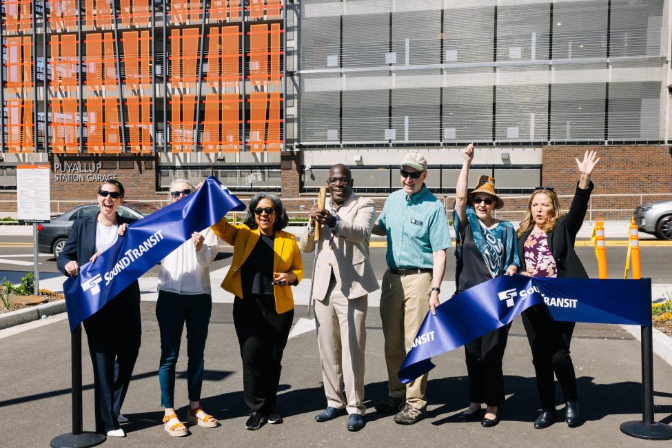 A group of people cut a blue ribbon outside the new parking garage at the Puyallup Sounder Station