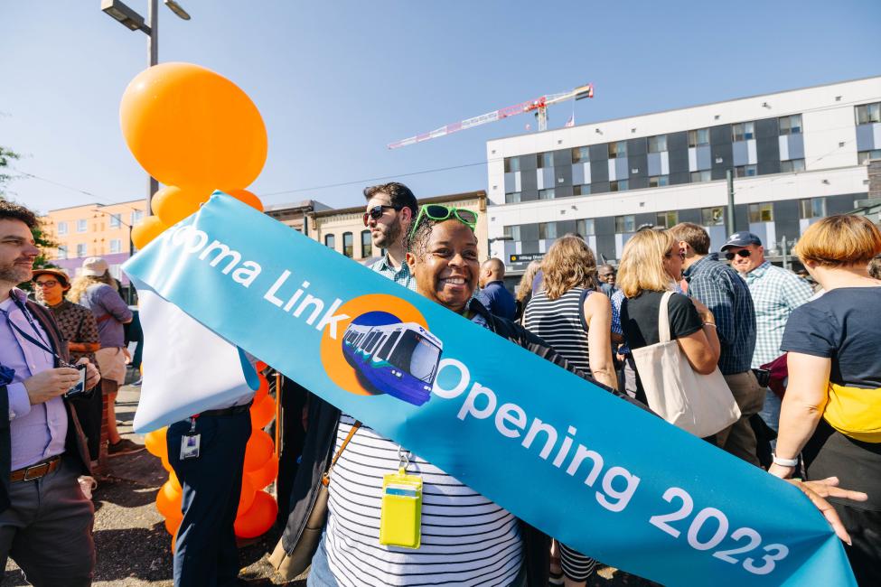 A person holds a teal blue banner that reads 'Tacoma Link opening 2023'