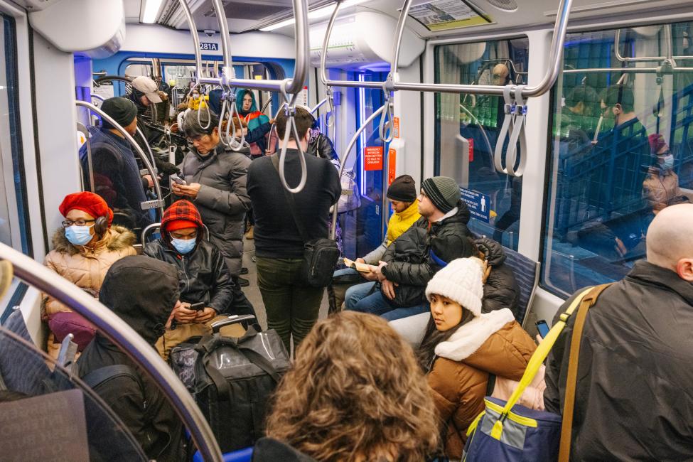 People sit and stand onboard a Link train. Some wear face masks.