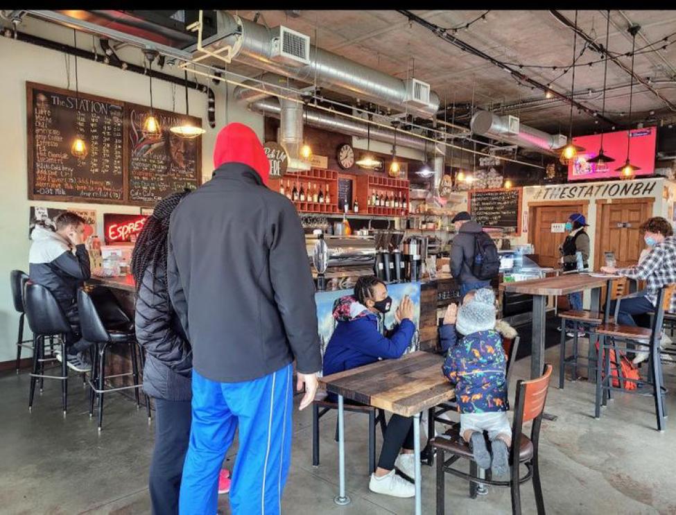 People stand and sit at tables in a coffee shop