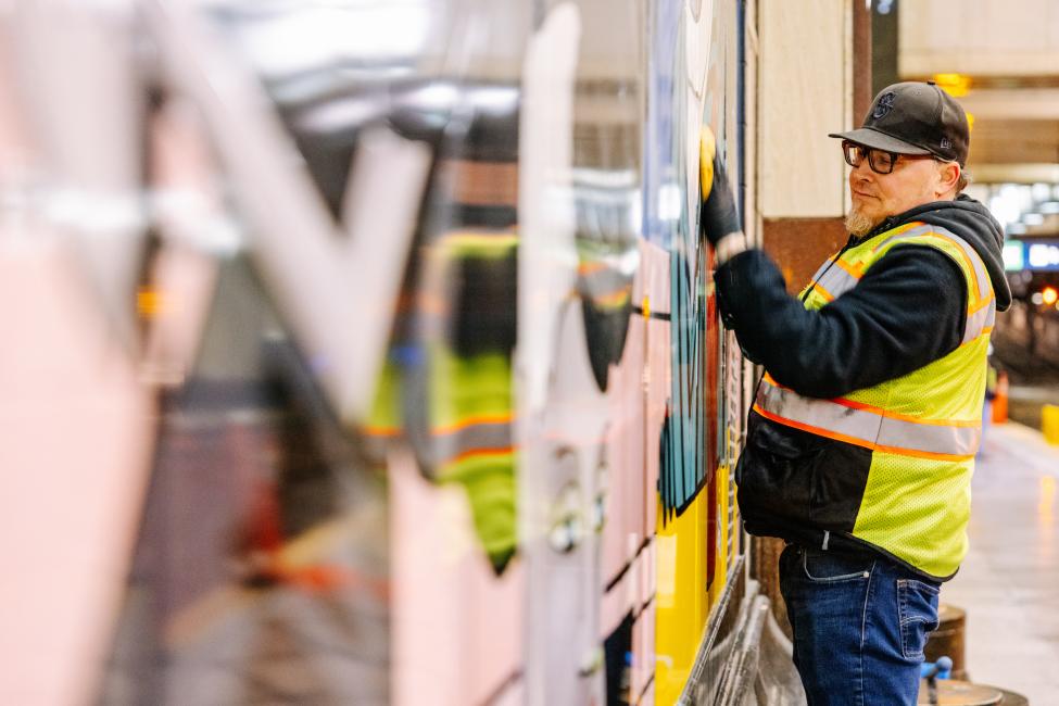 A worker cleans a piece of art on the wall at Westlake Station