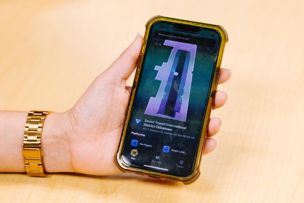 A hand holds a phone, with the screen showing a layout of a Link station on the GoodMaps app