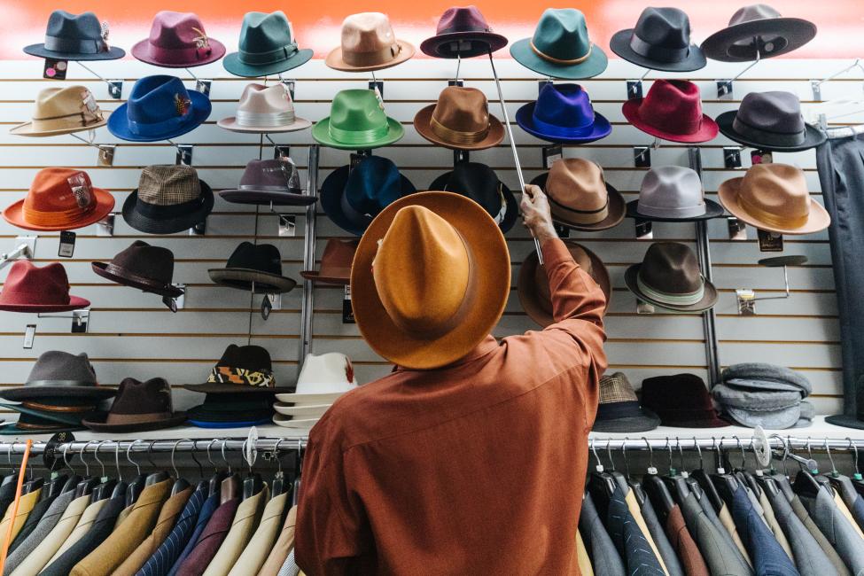 A customer selects from a large array of colorful dress hats lined on the wall.