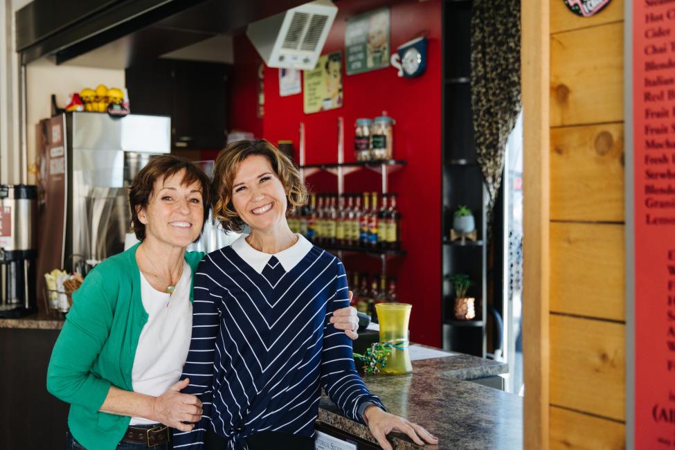 Two women hug with one hand and hold a cup of coffee in the other 