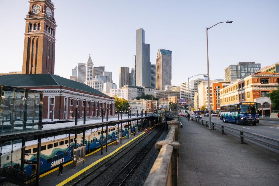 King Street Station on the left with a Sounder train at the platform, with Union Station, a street and an ST Express bus on the right