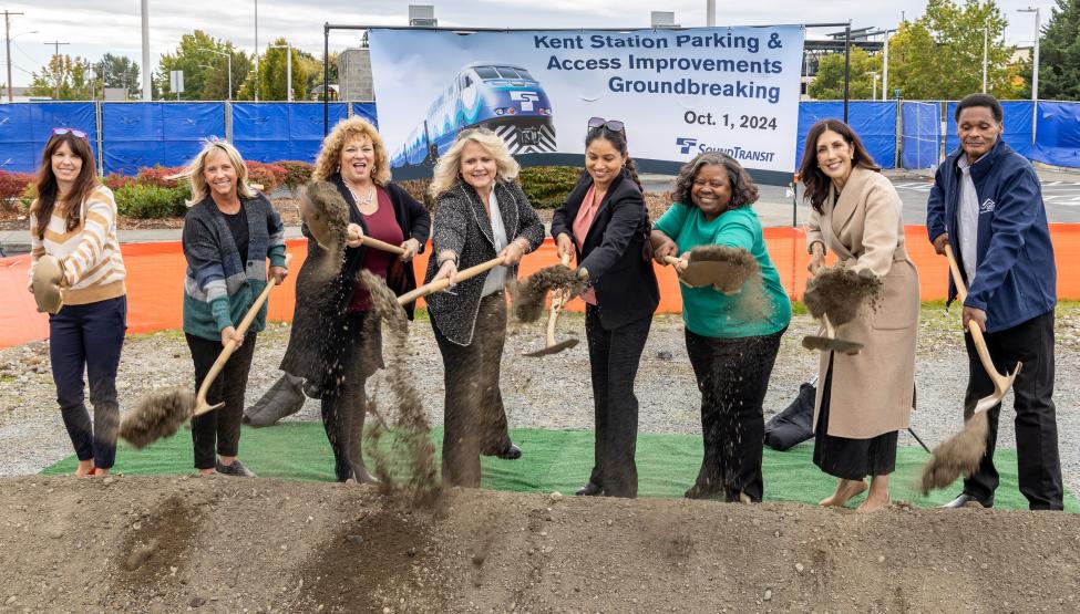 Eight people shovel dirt in a ceremonial groundbreaking in Kent for construction of a new parking garage for Sounder riders
