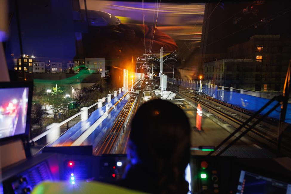 A view from behind a train operator's head of the Marymoor Village Station and parking garage
