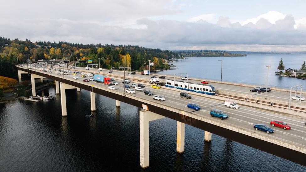 An aerial shot of the I-90 East Channel Bridge between Mercer Island and Bellevue. Cars and a Link light rail train cross the bridge on a sunny day.