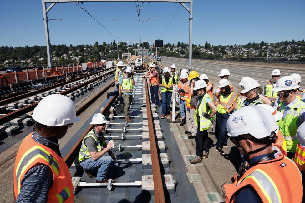 A group of people look at train tracks on the I-90 floating bridge
