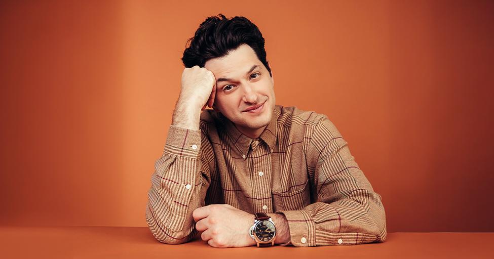 Ben Schwartz puts his hand on his head and looks directly at camera with an orange background