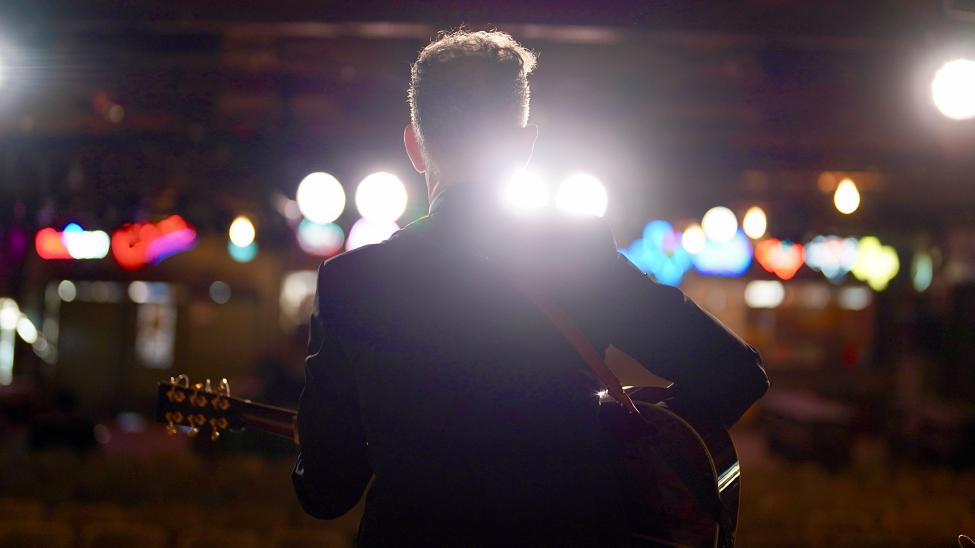 A silhouette shot of Lyle Lovett performing in front of a crowd