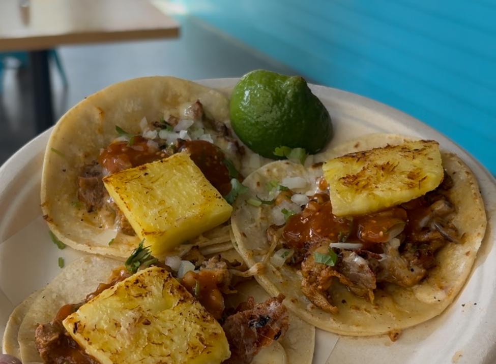 Three tacos on a plate with pineapple on top, and a lime on the side.