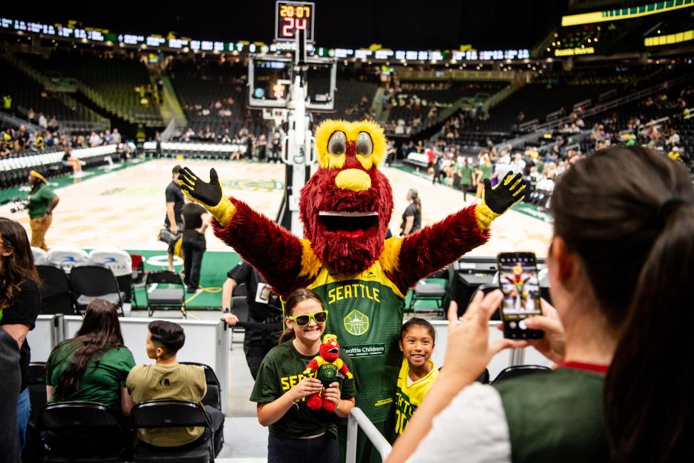 The Seattle Storm mascot, Doppler, raises their arms in front of a crowd at a basketball arena.