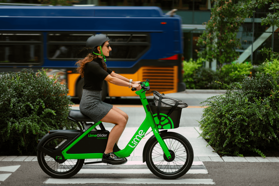 A woman rides a Lime Bike with a King County Metro bus going the opposite direction in the background.