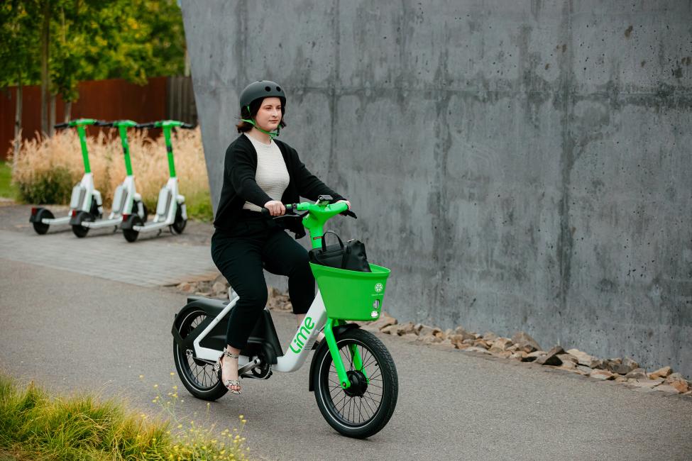 A woman rides a Lime Bike with a concrete wall and other Lime vehicles behind her.