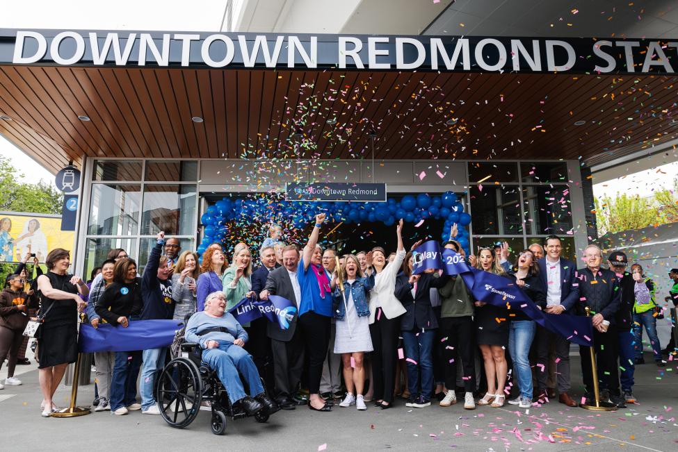 A group of people celebrates the ceremonial ribbon cutting as confetti falls at Downtown Redmond Station.