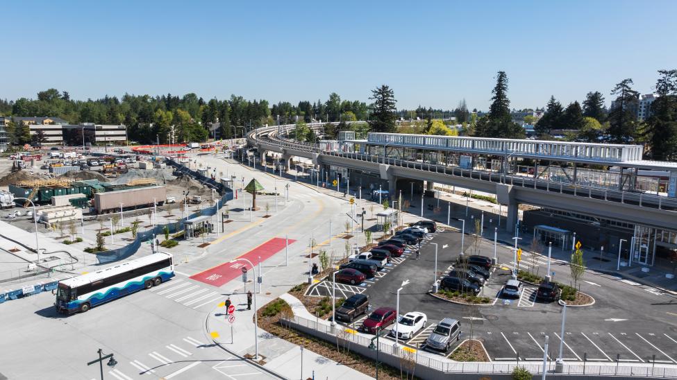 The light rail station in downtown Federal Way is nearing completion. Cars are parked at a lot by the elevated station, and an ST Express bus drives on a nearby road.