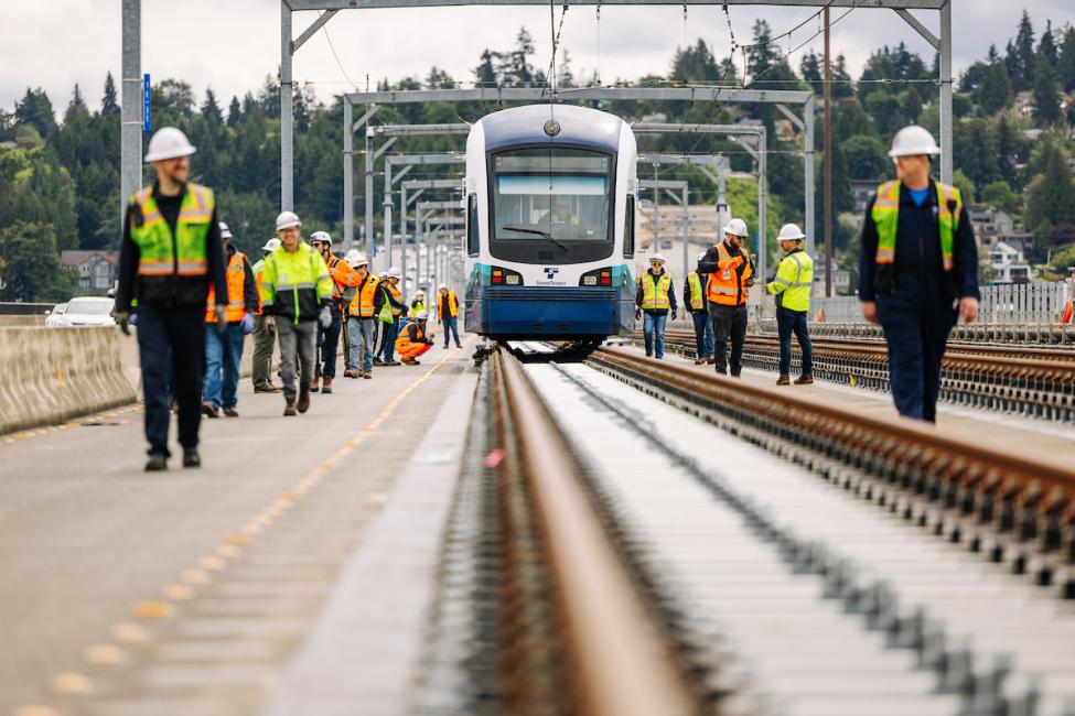 People in protective gear walk next to a Link light rail vehicle on the I-90 bridge during an unpowered tow test.