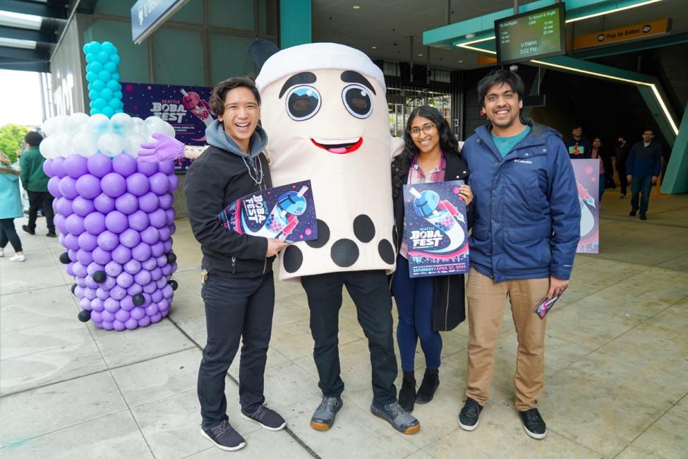 Three people pose with a mascot that looks like bubble tea