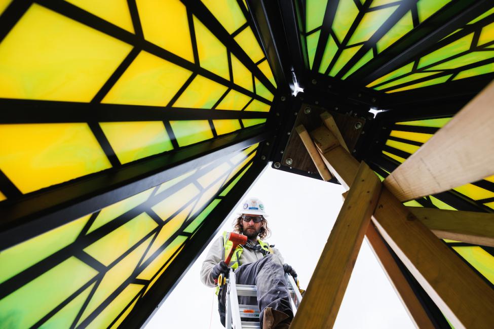 A worker peeks through a gap in an art installation resembling a larger-than-life stained glass lamp