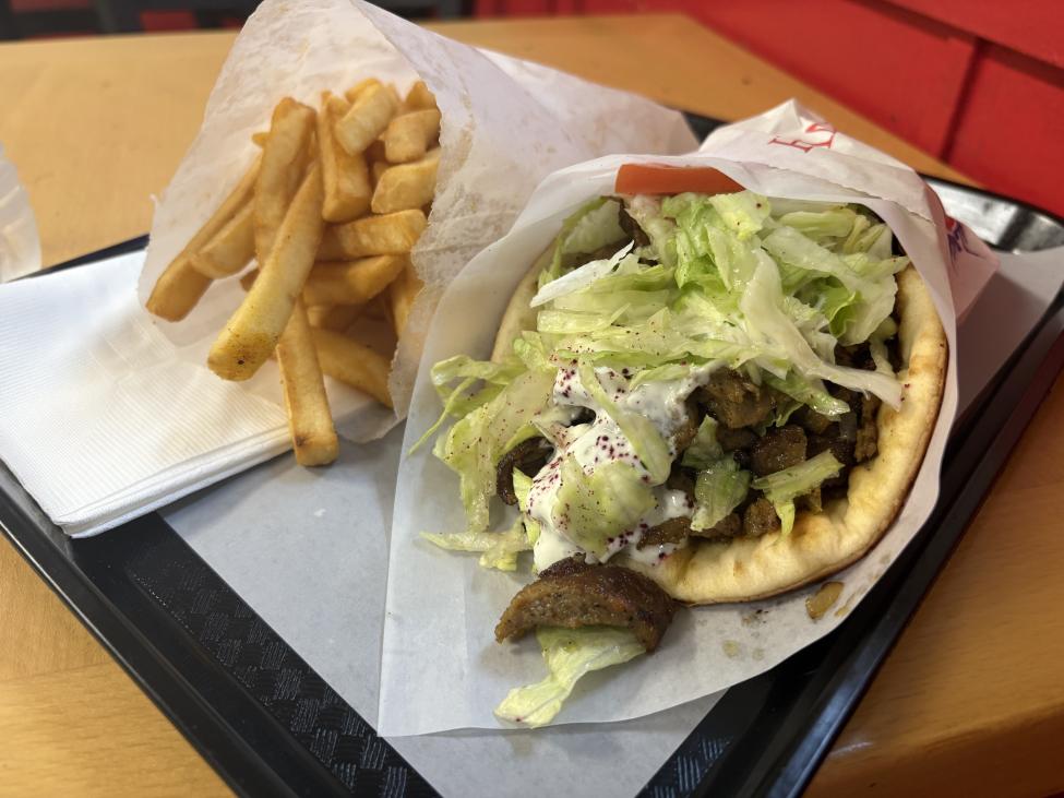 A gyro with lettuce and tomato and sauce on a red tray next to fries in a paper bag