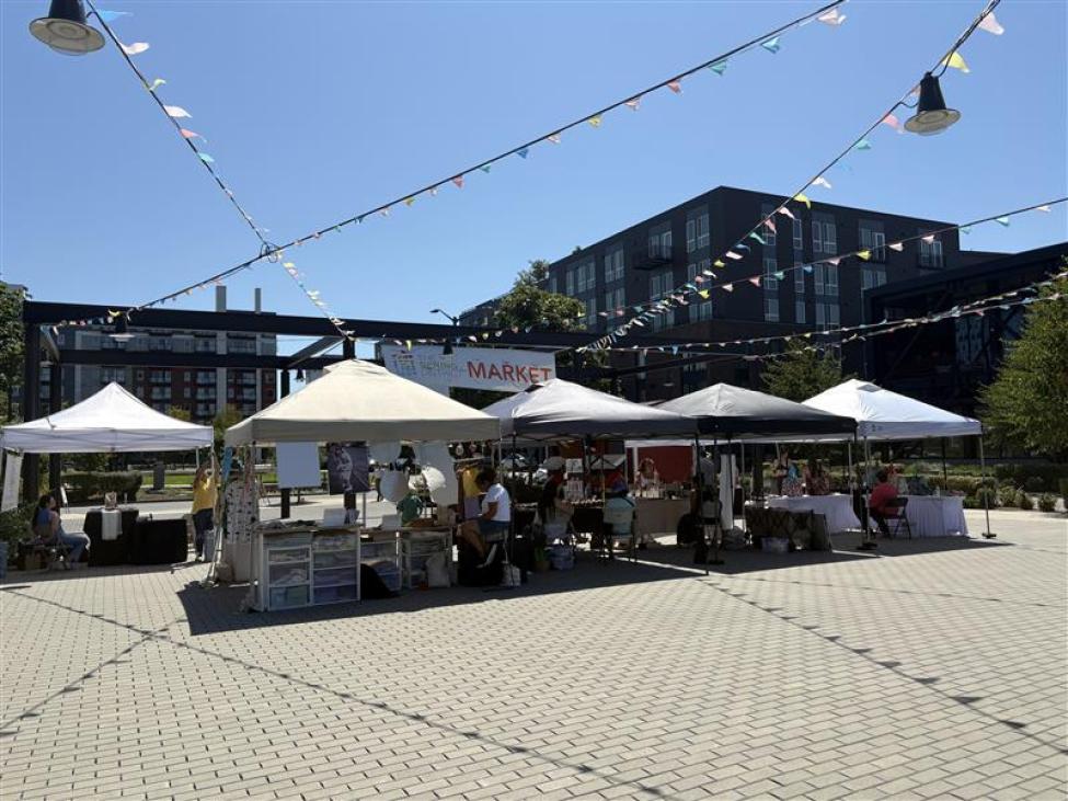 White tents with vendors on a sunny day in Bellevue. Flags hang above, as well as a large banner reading "Spring District market."