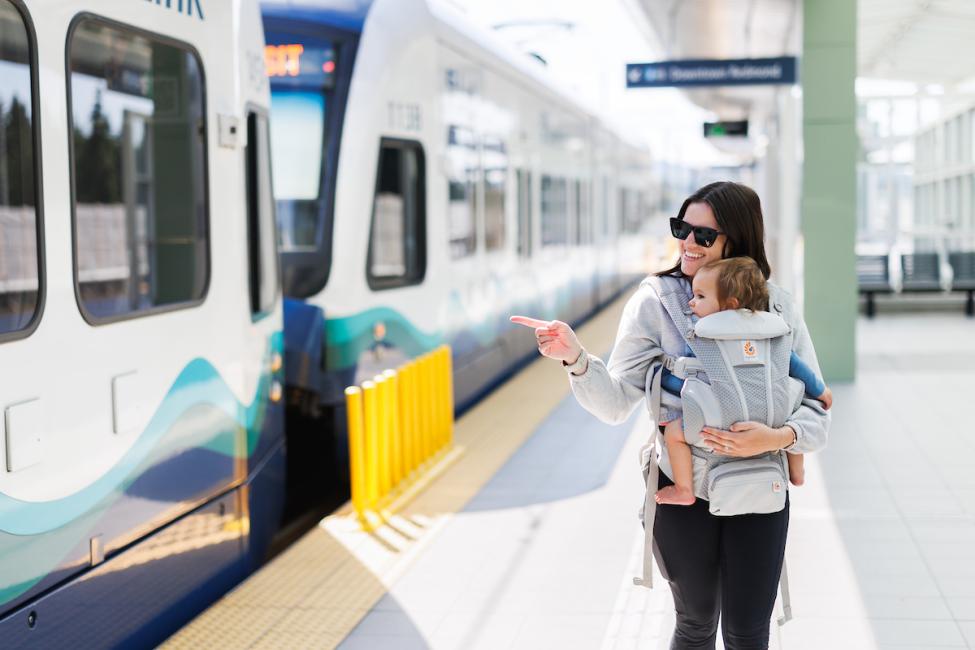 A mom holds her baby in a carrier while walking on a Link station platform