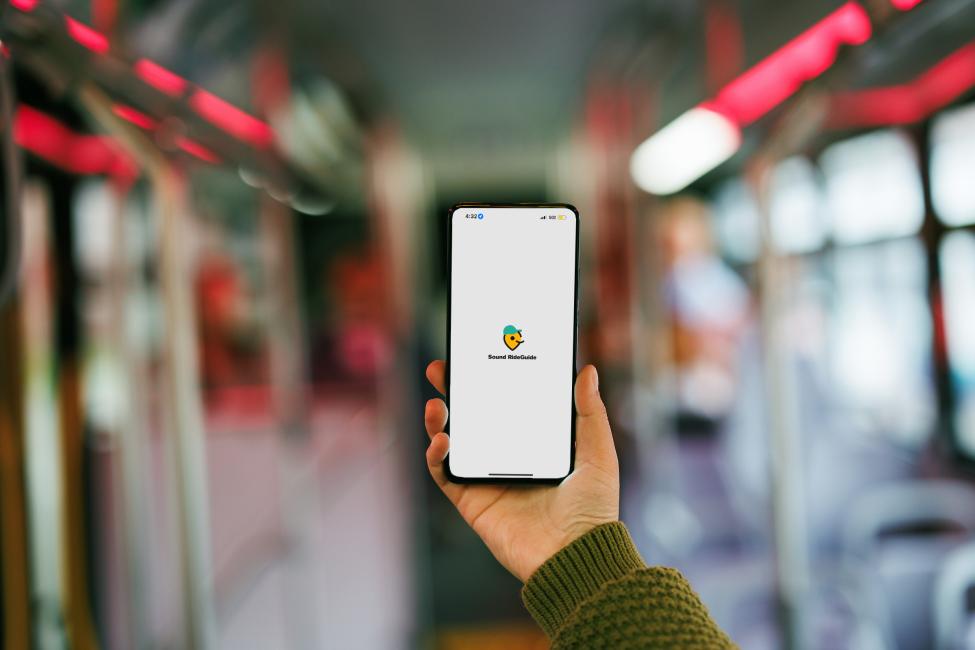 A hand holds a phone showing the new Sound RideGuide app logo