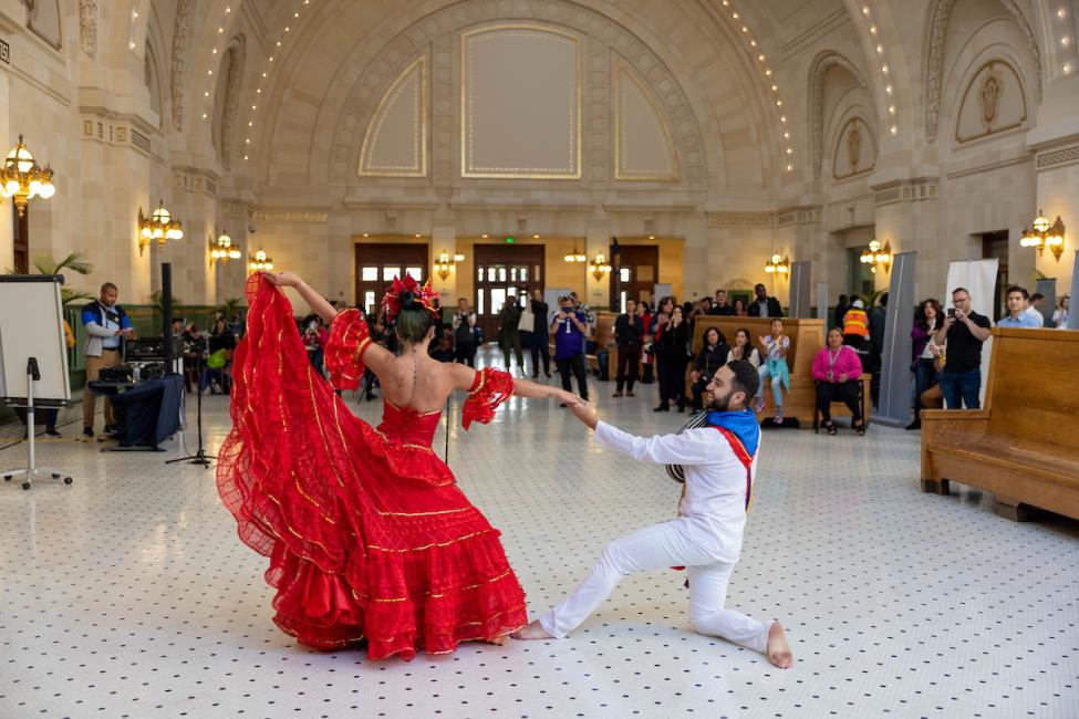 Two dancers - one in a long red dress and one in a white suit - perform for a crowd in Union Station