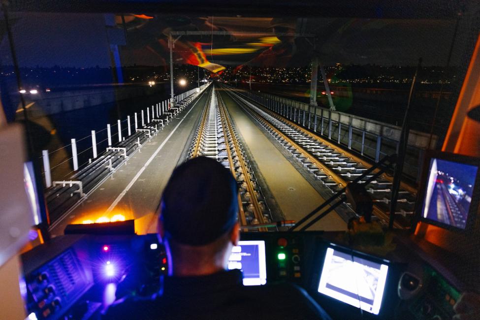The back of an operator's head in the cab of a Link train, with the view out of the front window behind them.