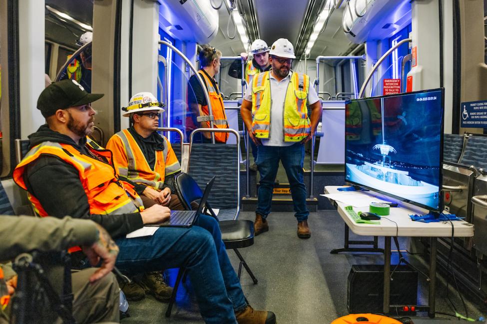 Five people wearing protective gear ride a Link train during nighttime testing.