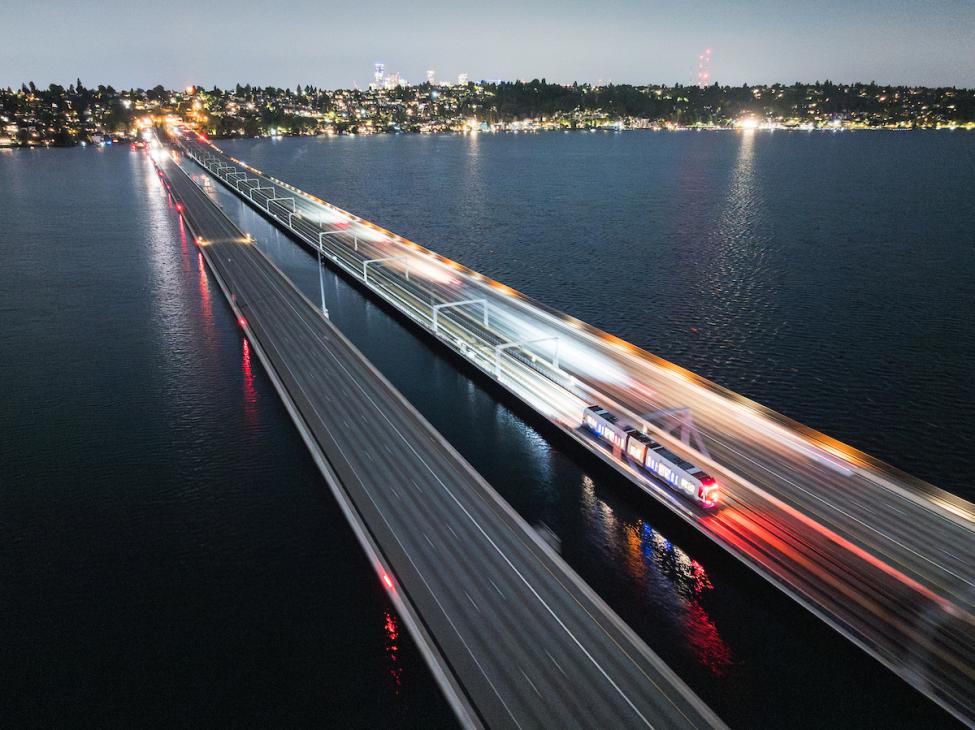An aerial shot of a one-car Link light rail train crossing the I-90 floating bridge at nighttime.