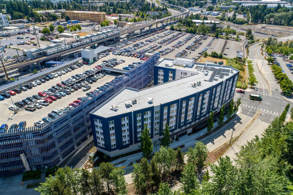 An aerial shot of a mixed-use building right next to the parking garage at Angle Lake Station, with a Link train on the platform in the background