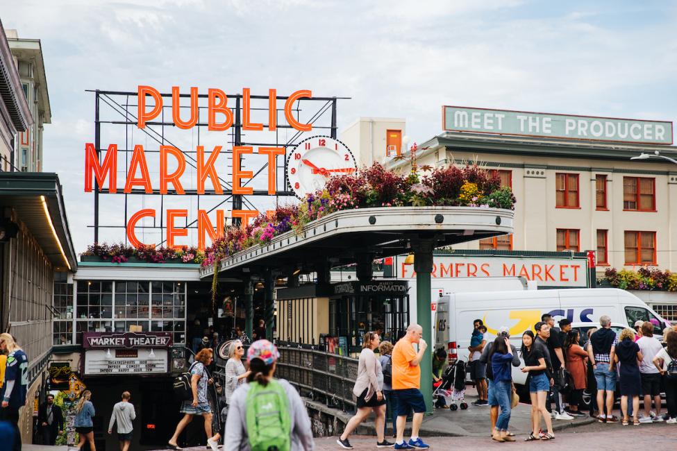 A bustling crowd of people walk through Pike Place on a sunny day