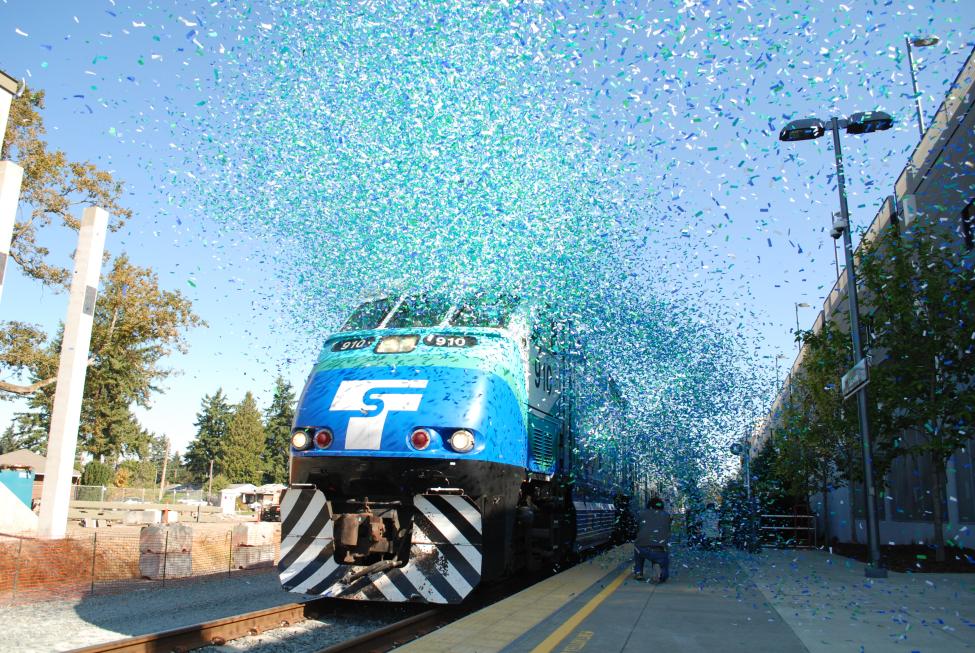 Blue and green confetti flies in front of a Sounder train