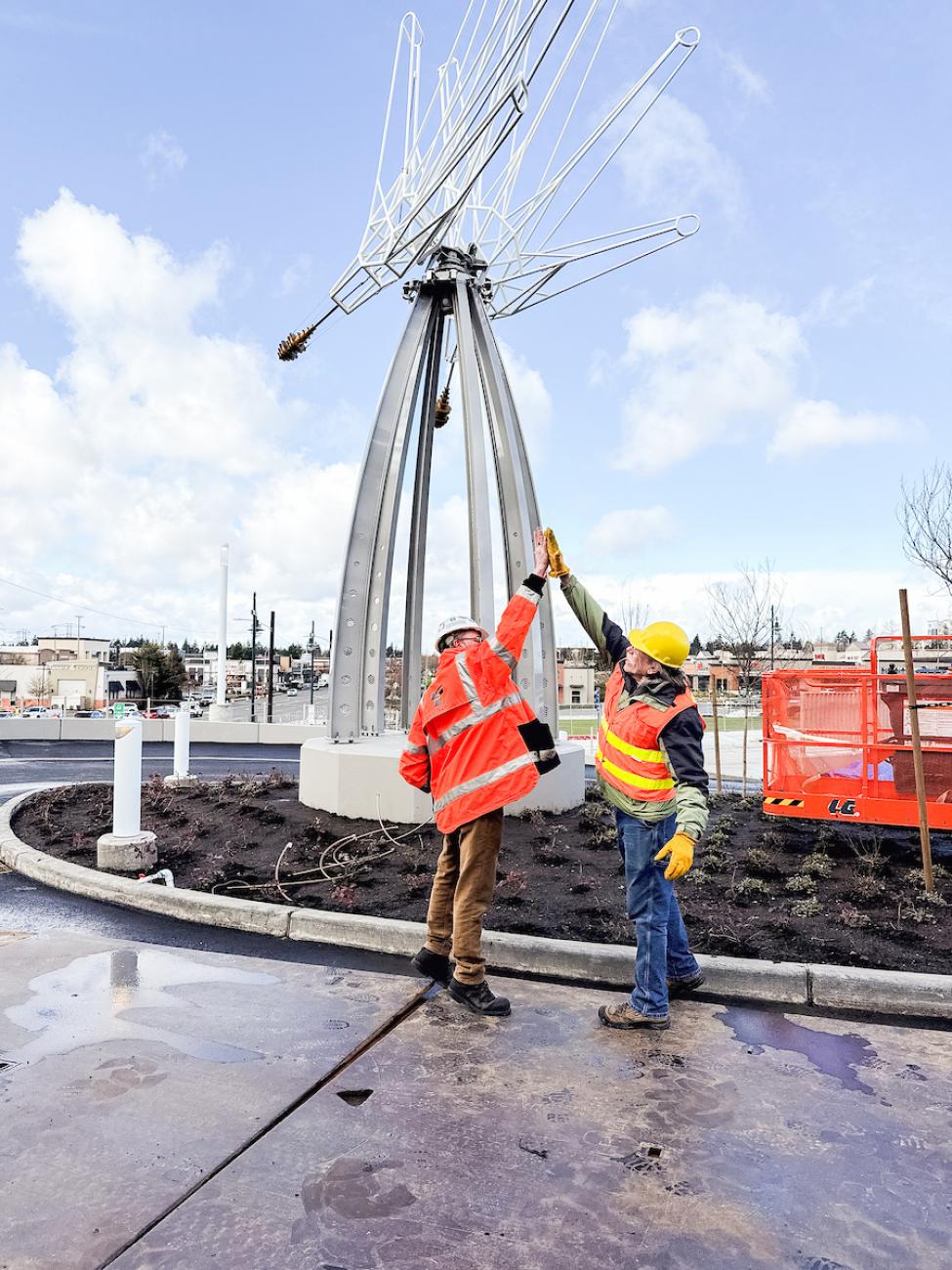 Two people in orange vests do a high five in front of a sculpture called Hi Five in Federal Way