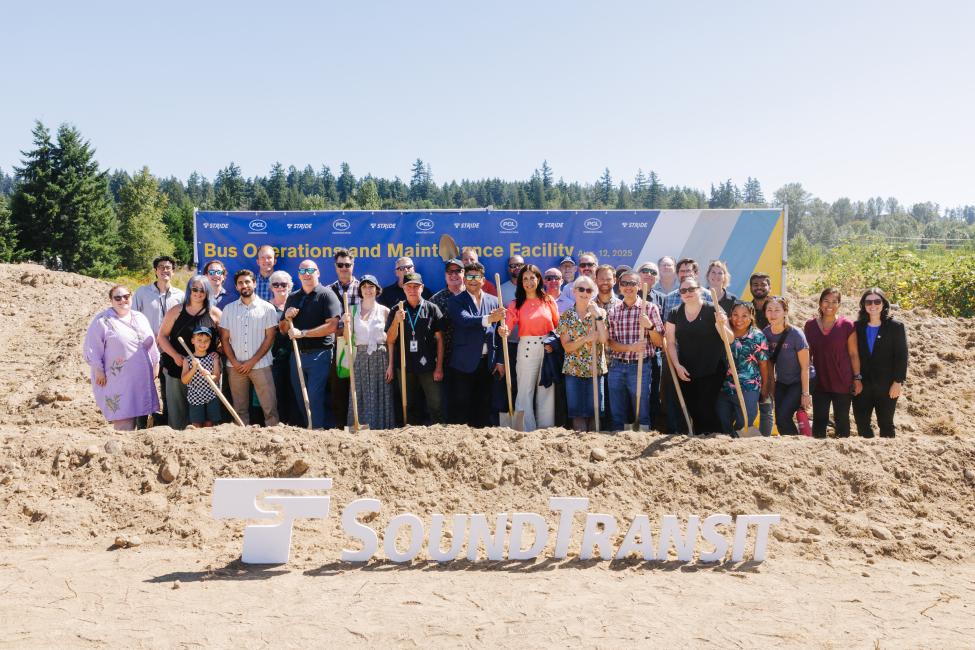 A group of about 30 people pose with golden shovels at the groundbreaking of a new bus base