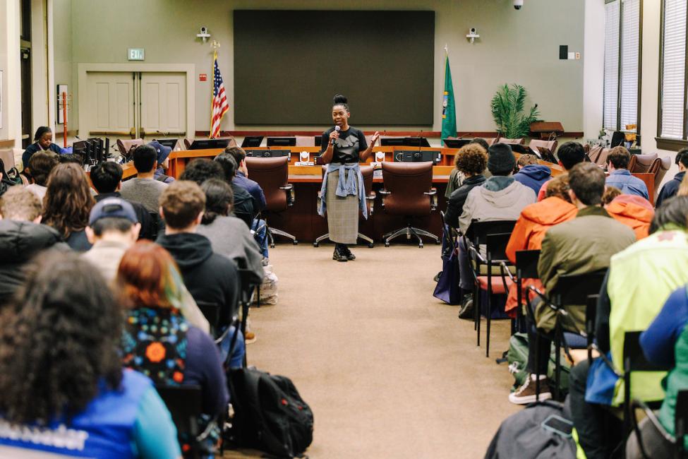 Nadia Anderson stands in front of a large group of young people in the Sound Transit boardroom.