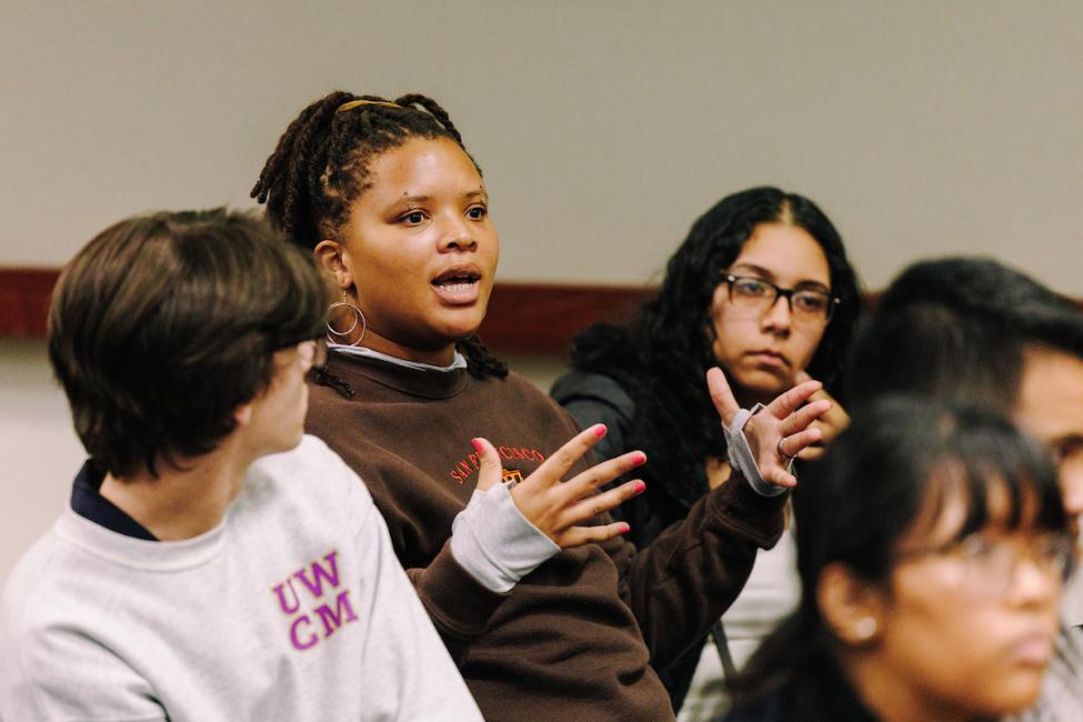 Three young people sit in chairs at the Sound Transit Youth Conference. One is asking a question.