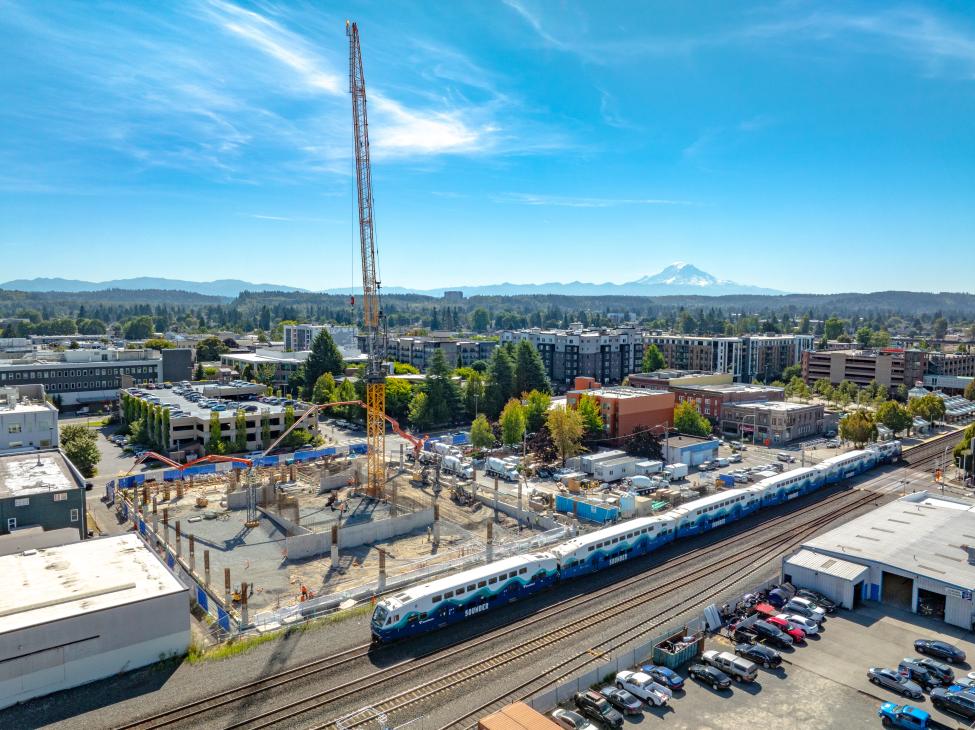 A Sounder train in the foreground, garage construction in the center and Mount Rainier in the distant background