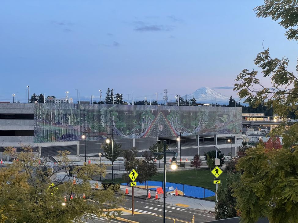 A large mural on the side of the parking garage in Federal Way at dusk, with Mount Rainier in the background of the photo