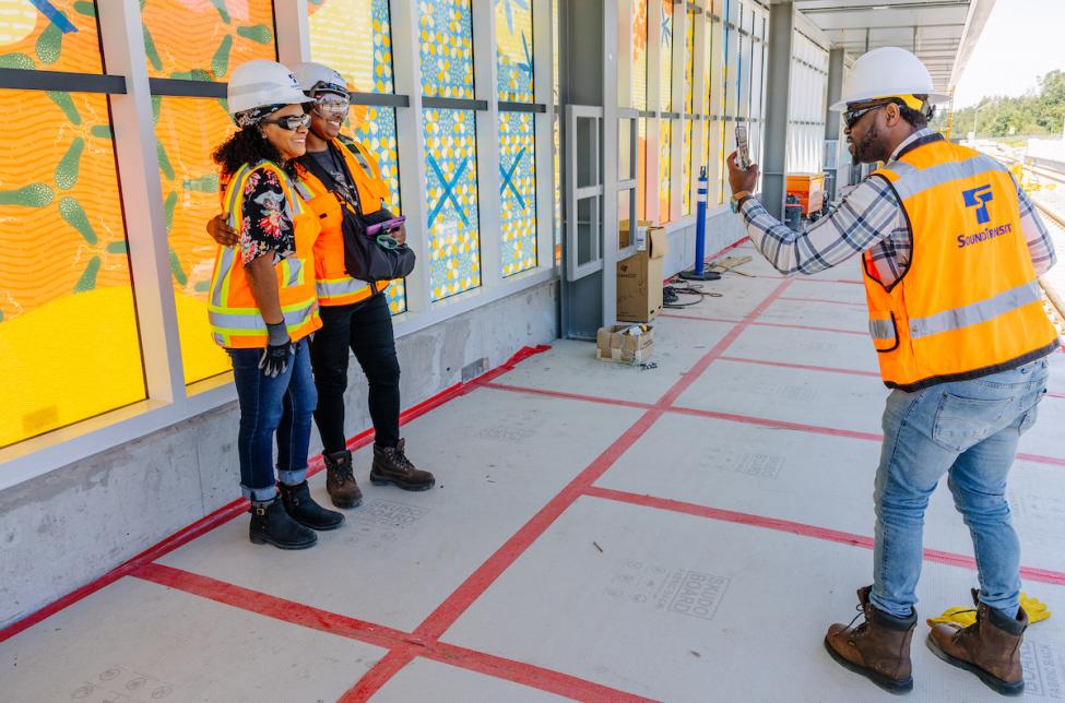 Two people in protective gear smile for a photo on the Star Lake platform as a third person takes their photo